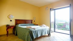 Helles Zimmer mit mediterranem Flair, gemütlichem Doppelbett und direktem Zugang zum Balkon mit Ausblick ins Grüne.