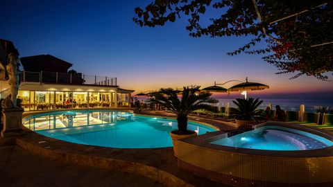 Stimmungsvolle Abendkulisse am beleuchteten Pool mit Whirlpool, gemütlichen Sitzplätzen und Blick auf den farbenprächtigen Sonnenuntergang über dem Meer.