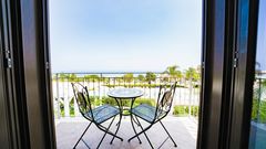 Balkon mit zwei Eisenstühlen und Tisch, Blick auf Poolanlage und das Meer in der Ferne.
