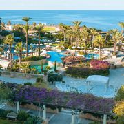 Großzügige Hotelanlage mit mehreren Pools, Palmen, weißen Sonnenschirmen und Meerblick – eine mediterrane Oase zum Entspannen.